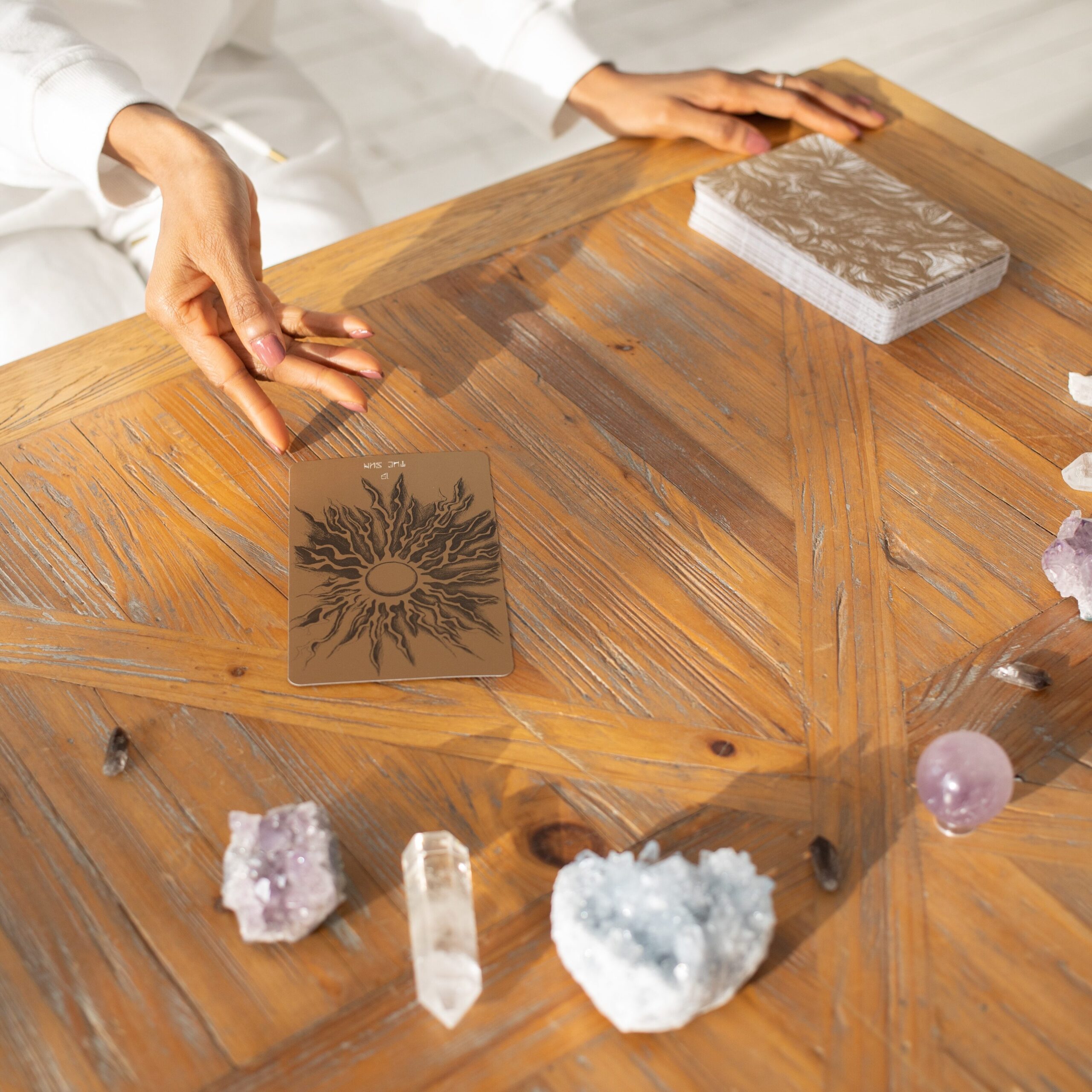 Wooden tabletop with several crystal stones and oracle cards spread out in front of woman. 