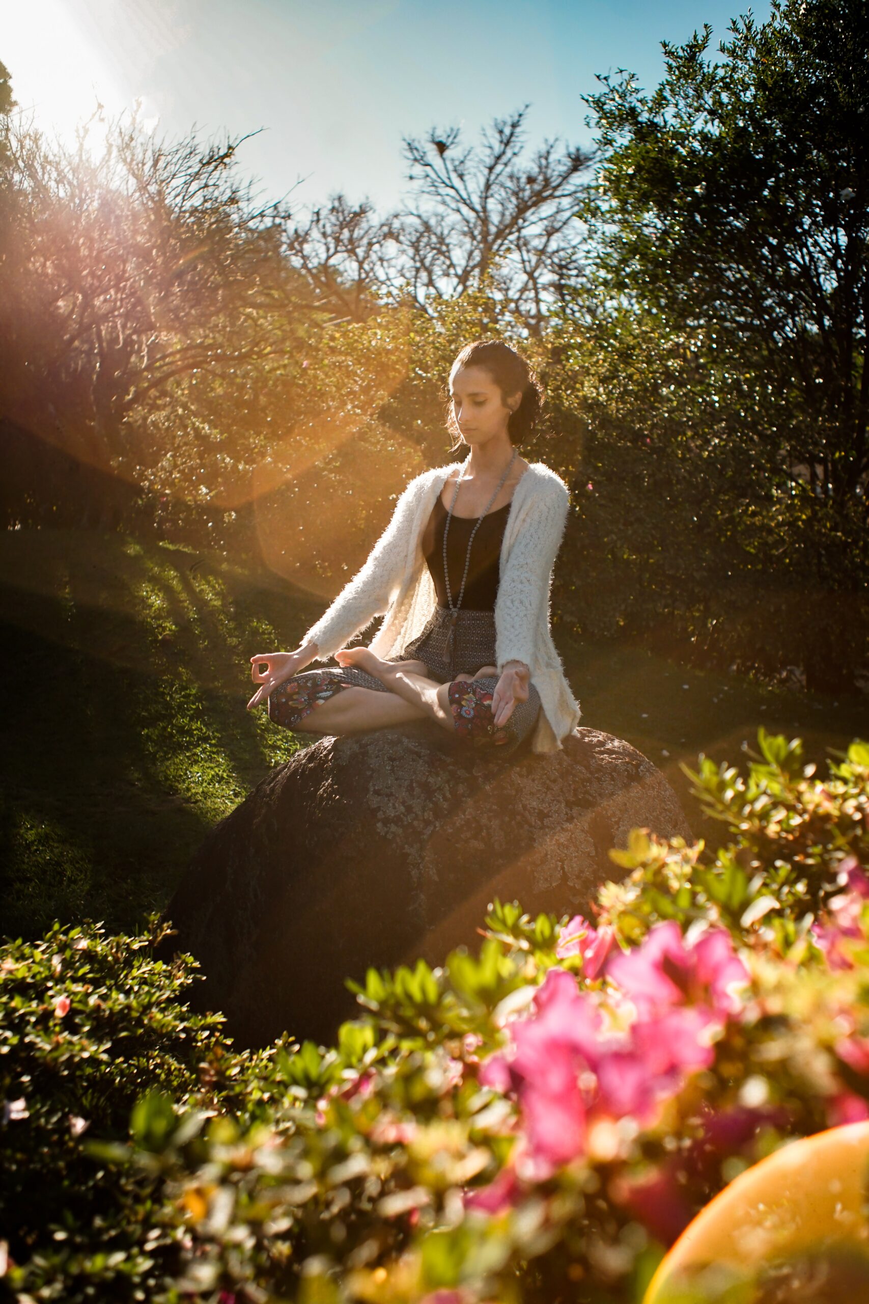 Woman sitting on large rock in forest-like area in a meditative pose