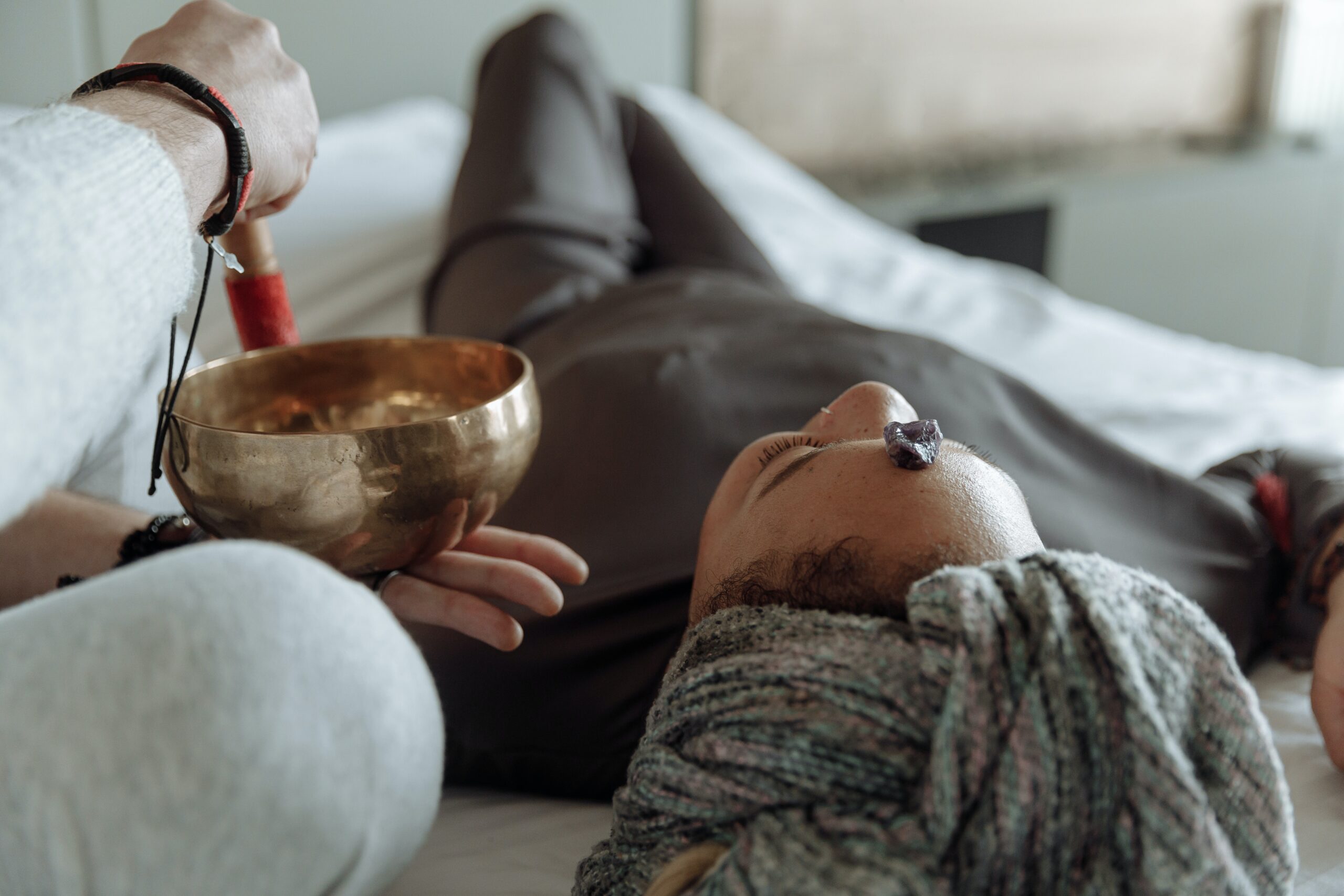 Woman lying on a massage table with a person ringing a sound bowl next to her